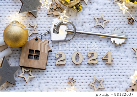 House key with keychain cottage on festive knitted background with stars, lights of garlands. Happy New Year 2024-wooden letters, greeting card. Purchase, construction, relocation, mortgage House key with keychain cottage on festive knitted background with stars, lights of garlands. Happy New Year 2024-wooden letters, greeting card. Purchase, construction, relocation, mortgage 98182037