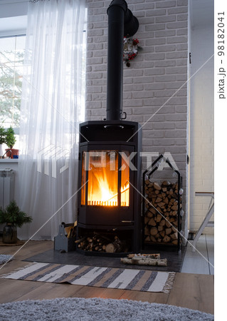 Black stove, fireplace in interior of house in loft style. Alternative eco-friendly heating, warm cozy room at home, burning wood Black stove, fireplace in interior of house in loft style. Alternative eco-friendly heating, warm cozy room at home, burning wood 98182041