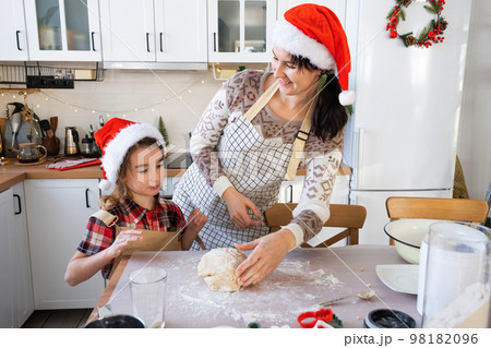 Mom and daughter in the white kitchen are preparing cookies for Christmas and new year. Family day, preparation for the holiday, learn to cook delicious pastries, cut shapes out of dough with molds Mom and daughter in the white kitchen are preparing cookies for Christmas and new year. Family day, preparation for the holiday, learn to cook delicious pastries, cut shapes out of dough with molds 98182096