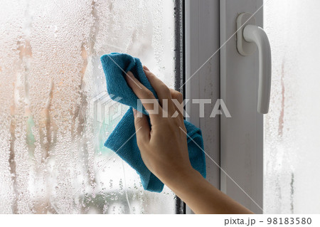 A womans hand wipes the condensate from the window glass with a towel. 98183580