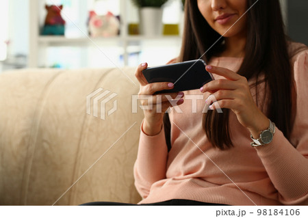 Woman sits on sofa and looks at smartphone closeup Woman sits on sofa and looks at smartphone closeup 98184106