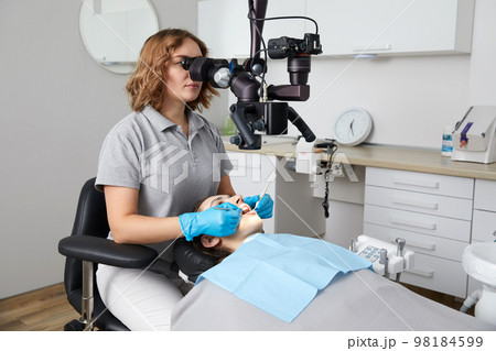 Female dentist with dental tools and microscope treating patient teeth at dental clinic office. Medicine, dentistry and health care concept. Female dentist with dental tools and microscope treating patient teeth at dental clinic office. Medicine, dentistry and health care concept. 98184599