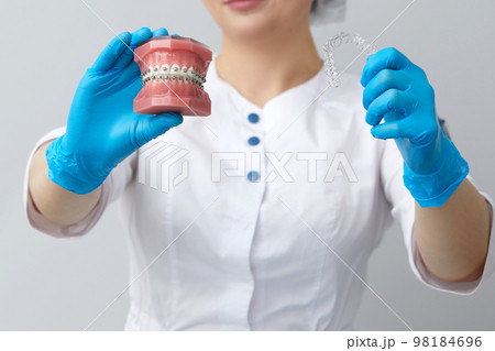 Orthodontist showing model of human jaw with wire braces and aligners explaining the difference 98184696