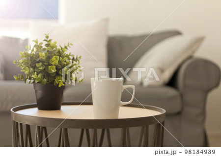 cup of hot tea. white mug on table near cozy gray sofa. pillows and blanket. Home relax Lifestyle 98184989