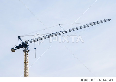 A tall construction crane with a long blue boom for moving building materials stands against a cloudless sky. 98186184