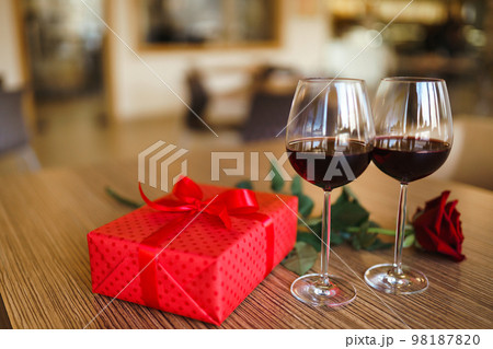 Valentine's day celebration concept. Two glasses of wine, red rose red gift box on wooden table. 98187820