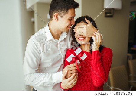 Young man gives his beloved a present and closes her eyes with a hand. Valentine's Day. Women's Day. Young man gives his beloved a present and closes her eyes with a hand. Valentine's Day. Women's Day. 98188308