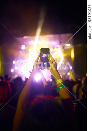 Hand with a phone records live music festival. People taking photographs with smart phone during concert. 98191088