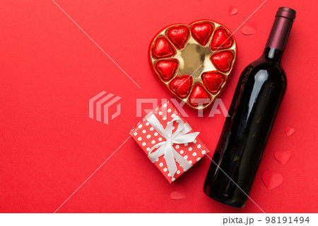Bottle of red wine on colored background for Valentine Day with gift and chocolate. Heart shaped with gift box of chocolates top view with copy space Bottle of red wine on colored background for Valentine Day with gift and chocolate. Heart shaped with gift box of chocolates top view with copy space 98191494