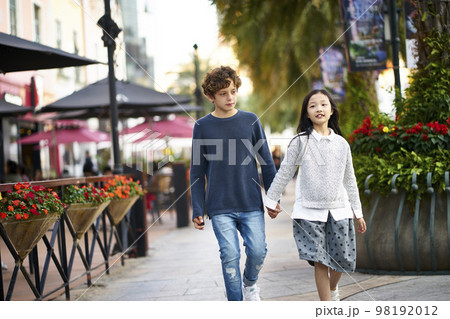 little asian girl and caucasian boy walking together holding hands outdoors little asian girl and caucasian boy walking together holding hands outdoors 98192012