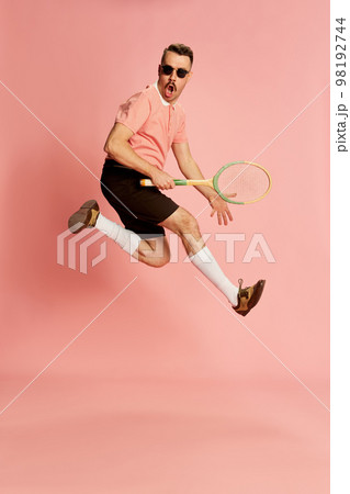 Portraits of handsome charismatic man in stylish clothes emotionally posing with tennis racket over pink studio background. Concept of fashion, sport, lifestyle 98192744