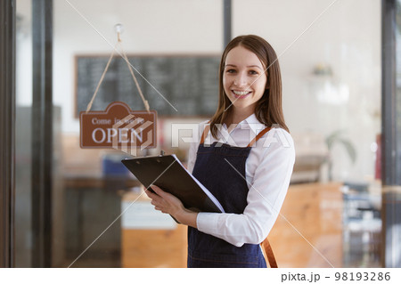 Young Female manager in restaurant with tablet. Woman coffee shop owner with open sign. Small business concept Young Female manager in restaurant with tablet. Woman coffee shop owner with open sign. Small business concept 98193286