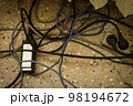 Electrical plugs with cords connected to power strip. Cable power cords in a tangled mess on floor of workplace, used dirty electric outlet 98194672