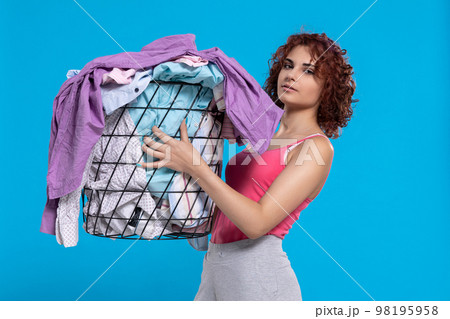 A girl with a sour face holding a basket of shirts in her hands. 98195958