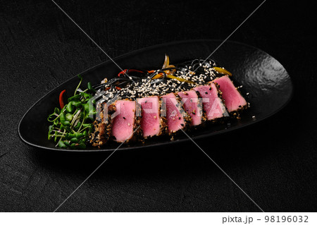 Baked tuna served with black noodles on black background Baked tuna served with black noodles on black background 98196032