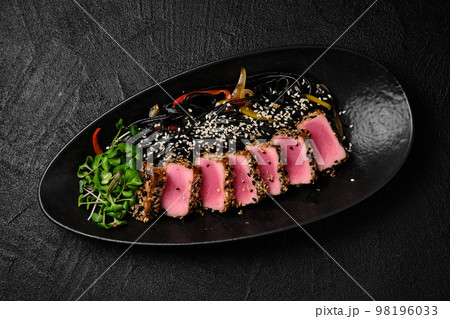 Baked tuna served with black noodles on black background Baked tuna served with black noodles on black background 98196033