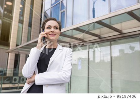 A portrait of a successful businesswoman speaking over a cell phone in the street. A manager, company employee A portrait of a successful businesswoman speaking over a cell phone in the street. A manager, company employee 98197406