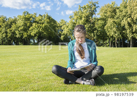 University student reading a book in the park on a sunny summer day. Concept - Education and knowledge 98197539