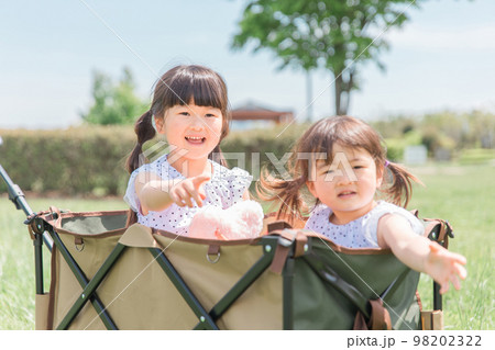 公園でキャリーカートに乗って遊ぶ姉妹の女の子（子供・幼児・少女） 98202322