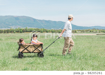 アウトドア・公園・草原でキャリーカート・ワゴンに乗って遊ぶ子供（女の子・キャンプ・パパ） 98205261