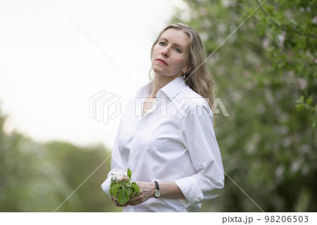 Elderly beautiful woman in a white shirt posing in a spring blooming garden. 98206503