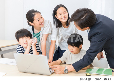 学校の授業でパソコンを使って勉強する小学生の子供達と先生（ICT教育・学校・塾・クラスメイト） 98213034