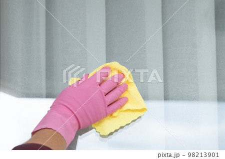 a hand in a pink glove washes a window with a yellow cloth on a sunny day. 98213901