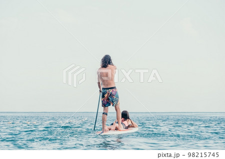 Sea woman and man on sup. Silhouette of happy young woman and man, surfing on SUP board, confident paddling through water surface. Idyllic sunset. Active lifestyle at sea or river. 98215745