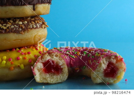 Yellow pink chocolate donuts lie a stack of a row of cut-off bitten doughnut stuffed with pink chocolate on a blue bright background with room for text. still life from food 98216474