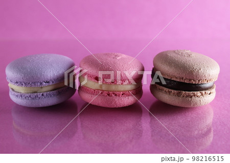 Three macaroons lilac brown chocolate lavender pink lie in a row on a pink fuchsia-colored background with reflection and a place for text and copyspace 98216515