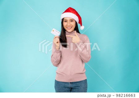 Cheerful beautiful Asian woman wearing red Christmas hat and holding mockup credit card 98216663
