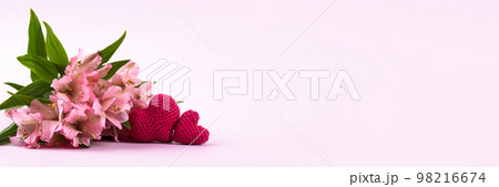 Composition of purple flowers Alstroemeria with a knitted pink hearts on a pink background. Valentine's Day concept, greetings for a loved one, top view, banner 98216674