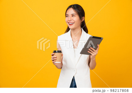 Business woman holding digital tablet and coffee cup with look sideways, light yellow background Business woman holding digital tablet and coffee cup with look sideways, light yellow background 98217808