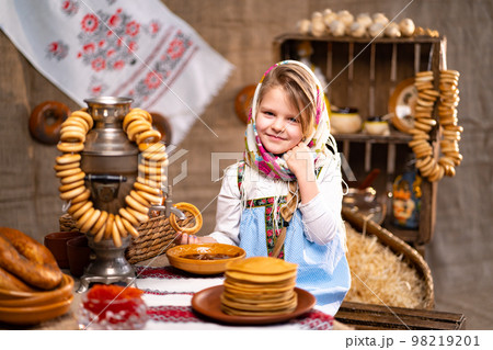 Little girl in folk Russian headscarf and dress with bagels and pancake celebrating Maslenitsa 98219201