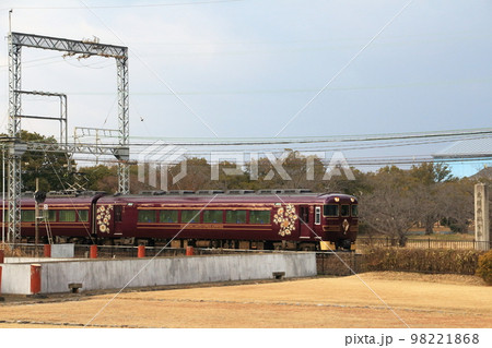 奈良平城宮跡内の復元遺跡横を駆け抜ける近鉄奈良線の電車 98221868