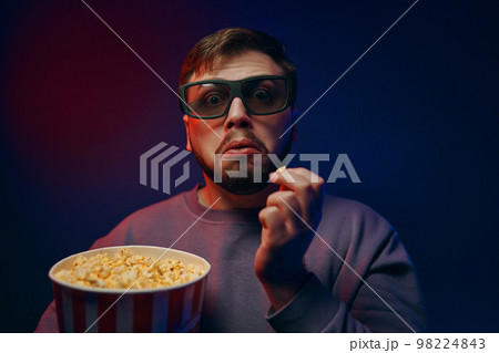 Watching a movie at home. A man watches a movie with a surprised expression on his face. Watching a movie at home. A man watches a movie with a surprised expression on his face. 98224843