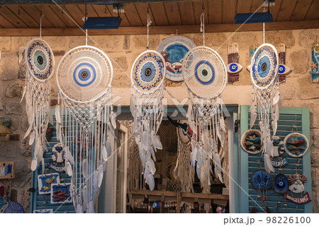 Dreamcatchers with evil eyes and feathers hanging from roof and souvenirs displayed on wall for sale at shop in Turkish market Dreamcatchers with evil eyes and feathers hanging from roof and souvenirs displayed on wall for sale at shop in Turkish market 98226100