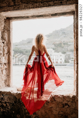 Redhead Woman in Red Dress posing in abandoned house. Curly redhead young caucasian Beautiful Girl in Long flying Cloth. Back view Portrait Redhead Woman in Red Dress posing in abandoned house. Curly redhead young caucasian Beautiful Girl in Long flying Cloth. Back view Portrait 98226327
