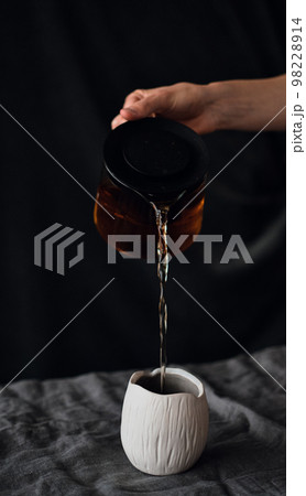 pouring tea from a teapot into an earthenware mug pouring tea from a teapot into an earthenware mug 98228914
