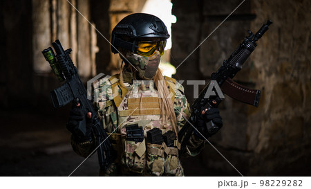 A woman in an army uniform holds a firearm in an abandoned building. A woman in an army uniform holds a firearm in an abandoned building. 98229282