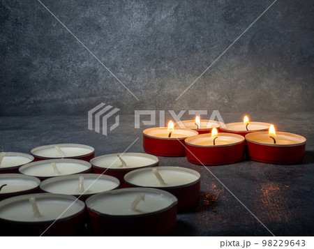 Short candles are burning on a dark background. Lots of small candles. Not all candles are lit. 98229643