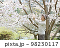 桜の枝を持ち上げて花を見ている笑顔のシニア女性　エプロン無し 98230117
