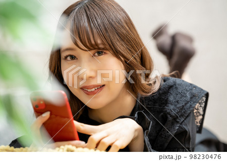 寝転んでスマホを使う若い女性 98230476