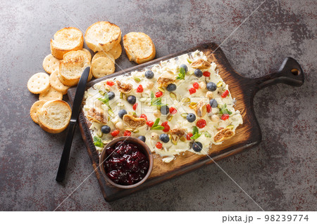 Flat lay of a butter board topped dried cherries and figs, pistachios, hazelnuts, fresh blueberries and mint served with toasts and crackers close-up. Horizontal top view 98239774