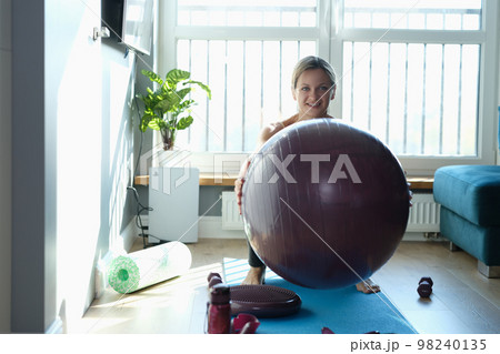 Woman exercising and doing squats with ball at home 98240135