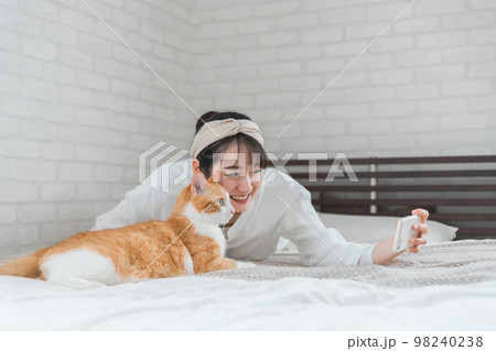 家のベッドルームでペットの猫とスマホで写真を撮って遊ぶアジア人女性 家のベッドルームでペットの猫とスマホで写真を撮って遊ぶアジア人女性 98240238