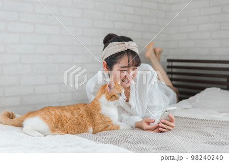 家のベッドルームでペットの猫とスマホで写真を撮って遊ぶアジア人女性 家のベッドルームでペットの猫とスマホで写真を撮って遊ぶアジア人女性 98240240