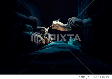 Closeup surgical team performing surgery to patient in sterile operating room. 98243019