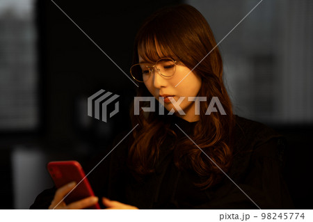 残業中にスマホを使う女性 98245774
