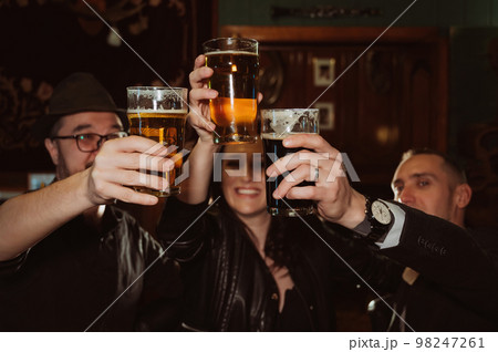 three happy friends happily clink glasses with beer behind bar counter 98247261